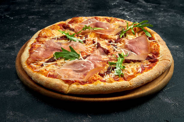 istock Pizza with jamon, arugula and sun-dried tomatoes on a black stone background. 45 degree angle view. Close-up, selective focus 1364395293
