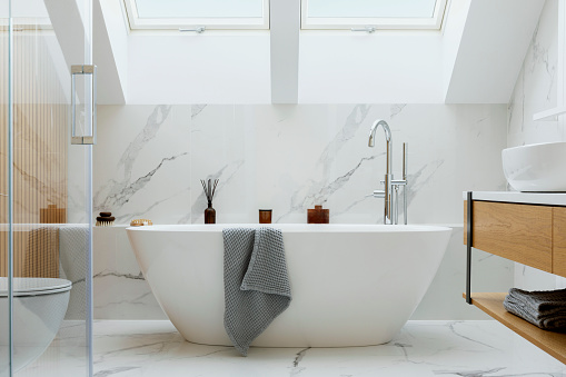 Elegante diseño interior de baño con paneles de mármol. Bañera, toallas y otros accesorios personales de baño. Concepto interior de glamour moderno. Ventana de techo. Plantilla