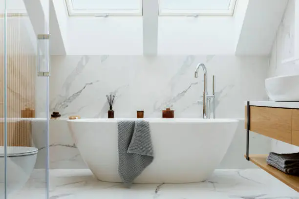 Photo of Stylish bathroom interior design with marble panels. Bathtub, towels and other personal bathroom accessories. Modern glamour interior concept. Roof window. Template.