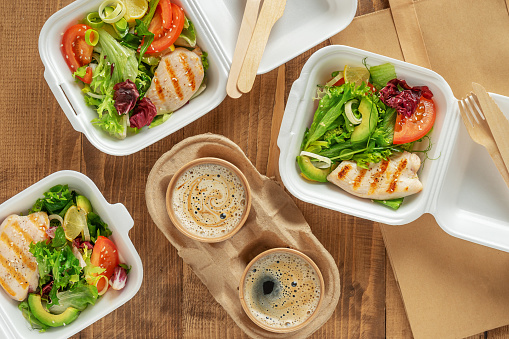 Takeaway food. Fresh salad with grilled chicken and coffee on wooden background. Top view.