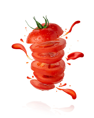 Flying sliced tomato with flowing splashes of ketchup isolated on white background with clipping path.