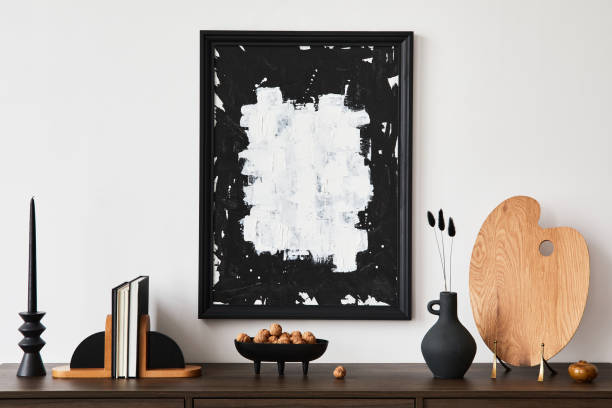 istock Creative composition of modern living room interior design with mock up poster frame, brown commode, books and personal accessories. White wall. Copy space. Template.