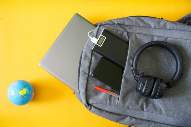 istock Modern gadgets smartphone, external battery and laptop lie in fashionable textile backpack next to  small globe. Yellow background. The concept of recharging gadgets while traveling and trip 1364398253