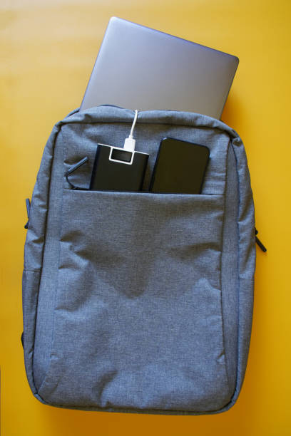 istock Gray textile city backpack containing silver laptop, smartphone and an external battery - power bank on a yellow background. Study, travel and trip with gadgets. Yellow gradient 1364398294