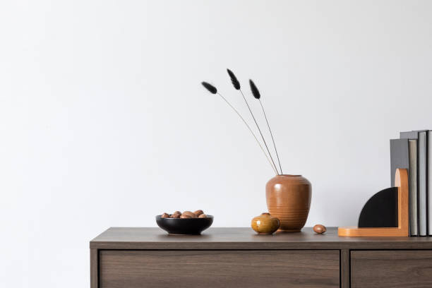 istock Minimalisitic composition of modern living room interior with brown commode, vases and accessories. White wall. Copy space. Template.