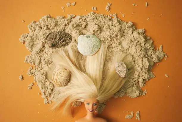 Blond with loose hair lie on the sand with hair full of shells. Flat lay.