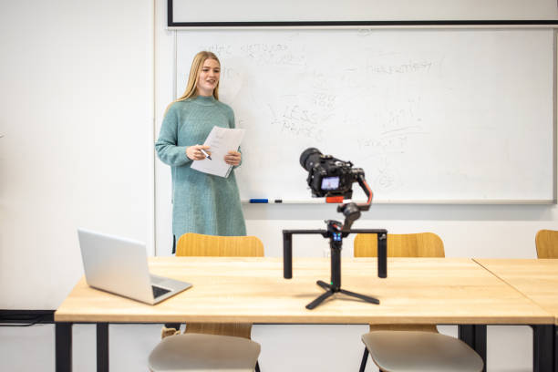 istock Female teacher  in front of whiteboard  recording lesson using video camera, as a new normal during coronavirus pandemic 1364400092