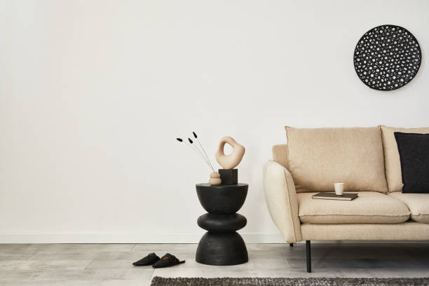 베이지 색 소파, 블랙 우드 사이드 테이블, 현대적인 홈 액세서리가있는 미니멀 한 거실 인테리어 디자인. 벽지. 공간을 복사합니다. 템플렛.  "n - designer living room brown white 뉴스 사진 이미지