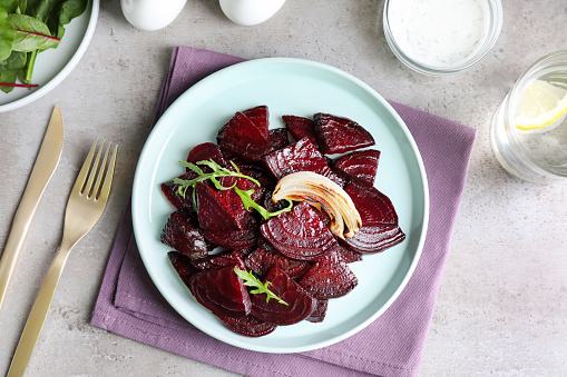 Roasted beetroot slices with onion and arugula served on light grey table, flat lay