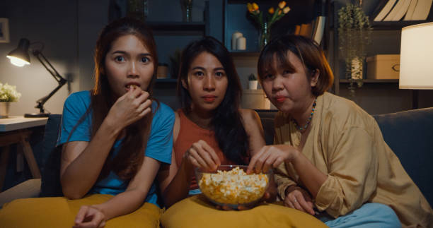 gruppo di attraente ragazza asiatica che impazzisce per la paura e il momento terrorizzato mangia popcorn guarda il film horror online sul divano in salotto a casa di notte. concetto di quarantena dell'attività di stile di vita del fine settimana. - freaking foto e immagini stock