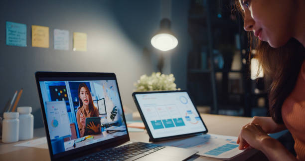 istock Asia woman using laptop talk to colleagues about work in video call while working from home at living room at night. Self-isolation, social distancing, quarantine for coronavirus prevention. 1364401703