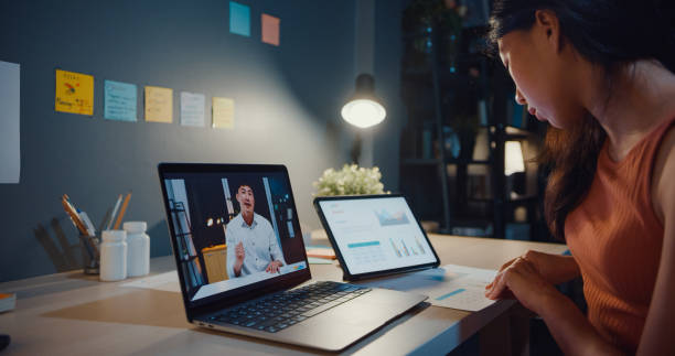 istock Asia woman using laptop see graph in table talk to colleagues about work in video call while working from home at living room at night. Self-isolation, social distancing, quarantine for coronavirus. 1364401737
