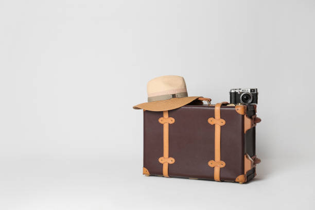 薄い灰色の背景に帽子とカメラを持つヴィンテージ旅行スーツケース、テキストのためのスペース。夏休み