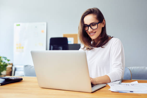 istock Happy young woman working with laptop at home 1364408376
