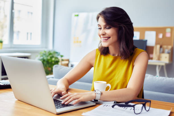 istock Smiling young business woman using laptop working from home office 1364408566