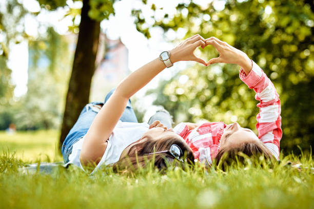 Two women lying on the grass making heart sign with hands