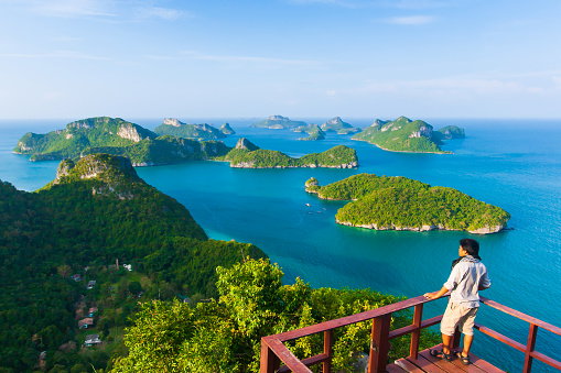 An Asian young man in casual wear stands at the terrace while relaxing islands view on sunny summer. Mu Koh Ang Thong National Park, tourist attractions in Thailand.