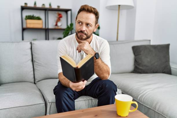 istock Middle age hispanic man reading book at home 1364412060