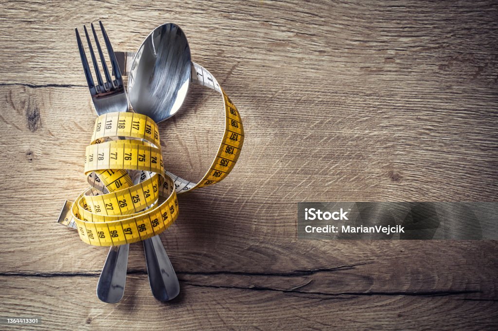 Spoon, fork and measuring tape on the kitchen table. The concept of a healthy diet Spoon, fork and measuring tape on the kitchen table. The concept of a healthy diet. Dieting Stock Photo
