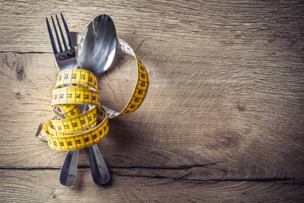 ложка, вилка и измерительная лента на кухонном столе. концепция здорового питания - похудение стоковые фото и изображения