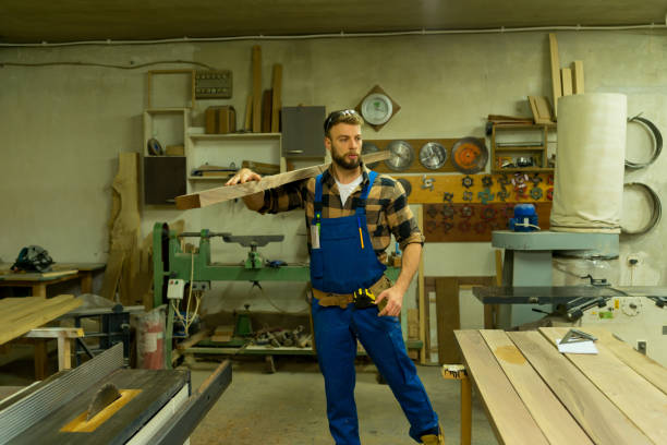 istock Handsome carpenter carries the long board through workshop 1364413440