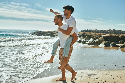 Lovely gay couple on piggyback ride at the beach.