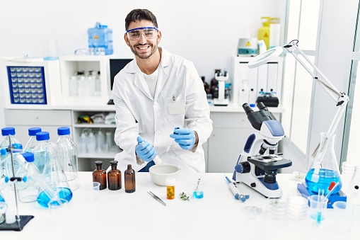 Handsome hispanic man using scientific mortar at laboratory