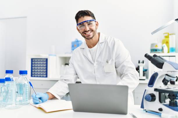 istock Handsome hispanic man working as scientific with microscope and laptop at laboratory 1364415771