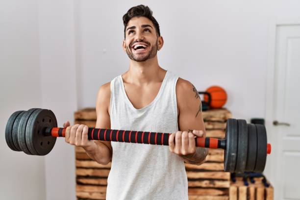 istock Young hispanic man training with weighs smiling and laughing hard out loud because funny crazy joke. 1364415917