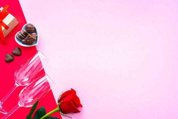 Valentine's Day or wedding background: red rose, Champagne glasses, chocolate candies and gift box shot on pink and red background. The composition is at the left of an horizontal frame leaving useful copy space for text and/or logo. High resolution 42Mp studio digital capture taken with SONY A7rII and Zeiss Batis 40mm F2.0 CF lens