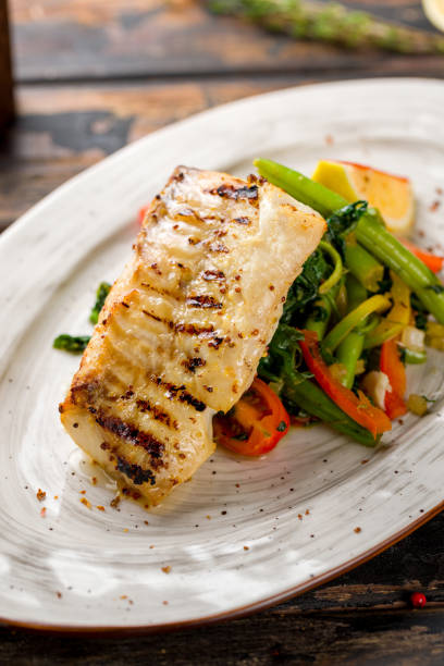 istock Grilled cod steak with fried vegetables on plate on wooden table macro close up 1364420570