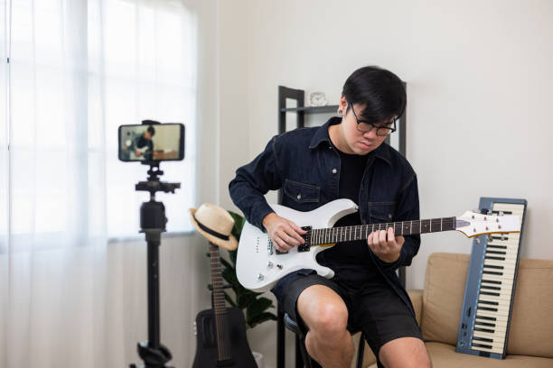 Young asian musician teaching the rock guitar class online live streaming on smartphone with student. Korean man playing electric guitar singing a song and record by cell phone shaed online social joven músico asiático que enseña la clase de guitarra rock en línea transmisión en vivo en teléfono inteligente con el estudiante. hombre coreano tocando la guitarra eléctrica cantando una canción y grabando por teléfono celular shaed online socia