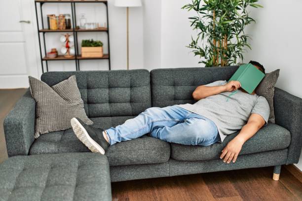 istock Young hispanic man sleeping with book on face lying on the sofa at home. 1364421659