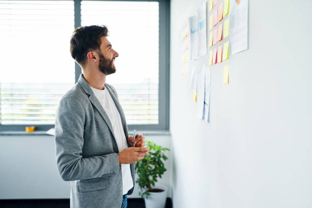 istock Cheerful young businessman looking at notes on office wall 1364422103