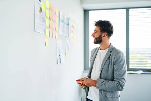 istock Smiling businessman looking at notes and documents posted on office wall 1364422132