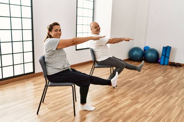 istock Middle age hispanic couple stretching using chair at sport center. 1364422253