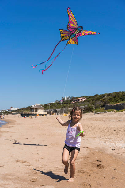 Little girl running with flying kite on the big deserted beach during a travel with family - Little girl playing with kite butterfly on sea shore in a spring sunny day Little girl running with flying kite on the big deserted beach during a travel with family - Little girl playing with kite butterfly on sea shore in a spring sunny day invertebrate photos stock pictures, royalty-free photos & images