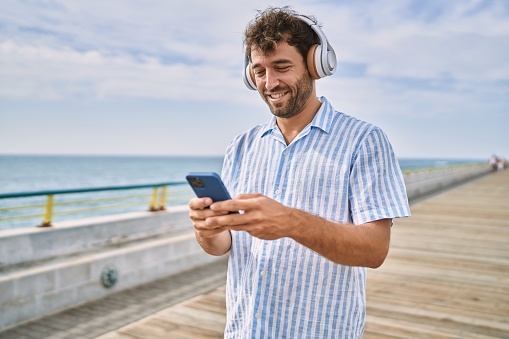 Young hispanic man smiling happy listening to music at the promenade.