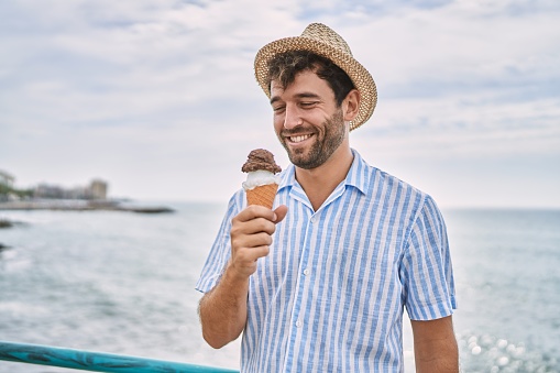 Young hispanic man smiling happy eating ice cream at the beach.