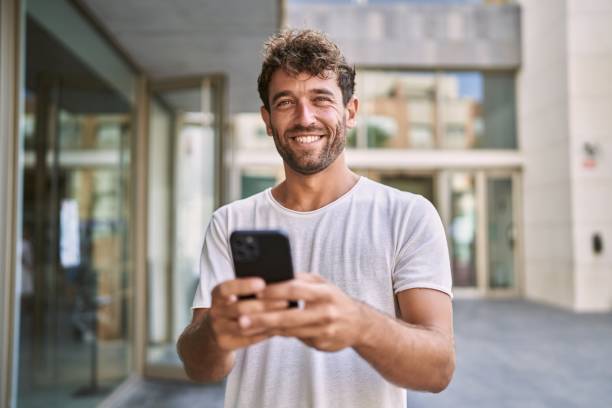 Young hispanic man smiling confident using smartphone at street stock photo