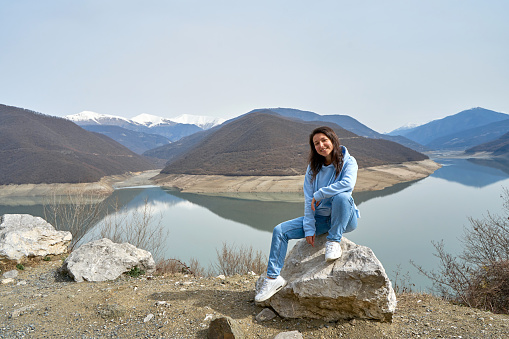 A girl poses against the background of the Zhinvali reservoir while traveling in Georgia. Incredible natural landscape.