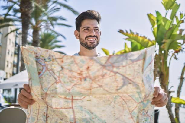 istock Young hispanic man smiling happy holding map at the city. 1364425894