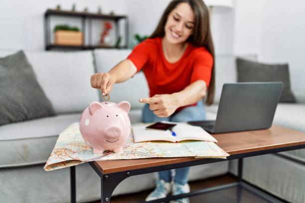 Young brunette woman putting euro coin in piggy bank saving for travel smiling happy pointing with hand and finger stock photo