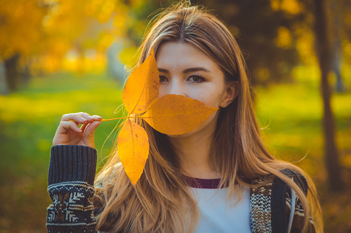 Portrait of beautiful woman holding the yellow leaf and covering the face