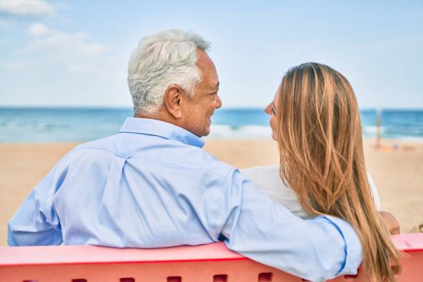 istock Middle age hispanic couple on back view sitting on bench at the beach. 1364436480