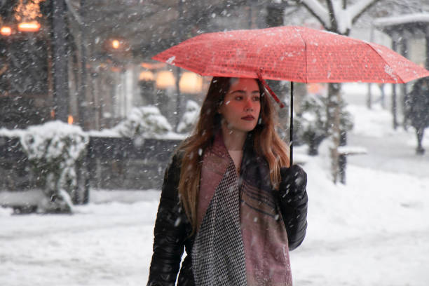 una joven caminando bajo un paraguas rojo en un día nevado de invierno en la ciudad - young women teenager teenagers only adolescence fotografías e imágenes de stock