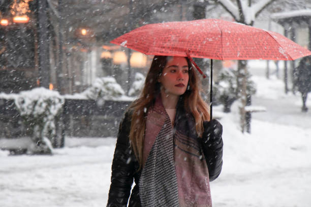 One young woman walking under red umbrella on a snowy winter day in the city stock photo