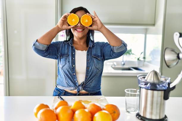 istock Hispanic brunette woman holding half oranges over eyes at the kitchen 1364445410