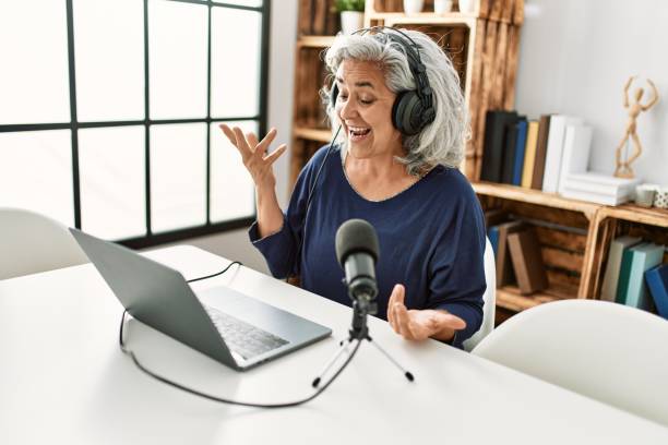 istock Middle age grey-haired woman smiling happy working at radio studio. 1364445838
