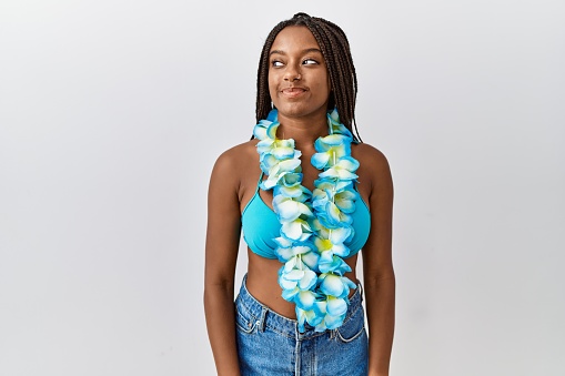 Young african american woman with braids wearing bikini and hawaiian lei smiling looking to the side and staring away thinking.